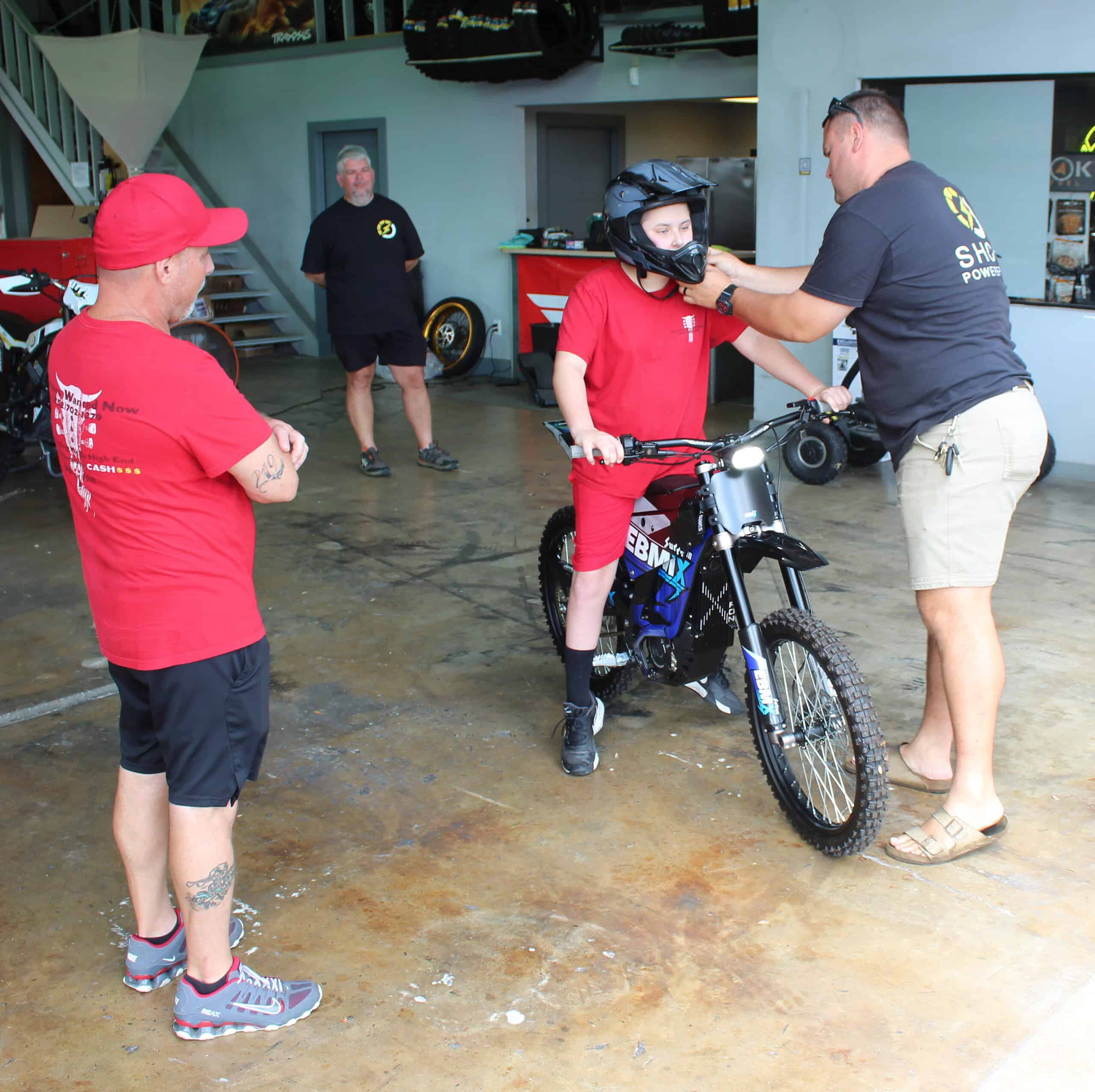 Aaron Nations (right) adjusts Deegan's helmet as he prepares to take his new electric motorbike out for a spin. His father, Anthony Giglio (far left) looks on. [Photo by Austyn Szempruch]