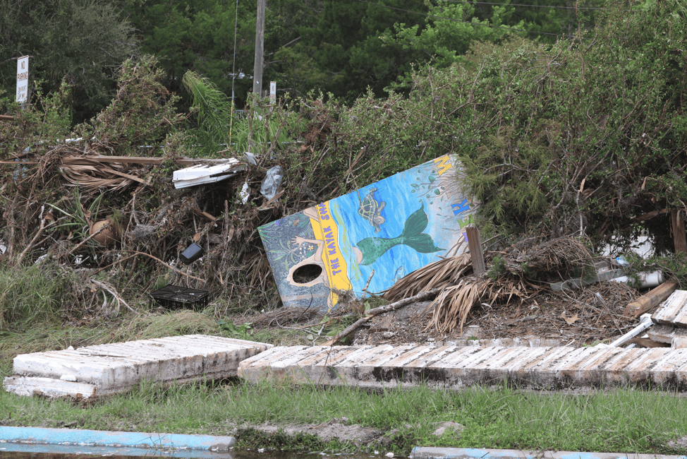 A sign from the Kayak shack sits with debris and broken pieces of dock. [Credit: Mark Stone]