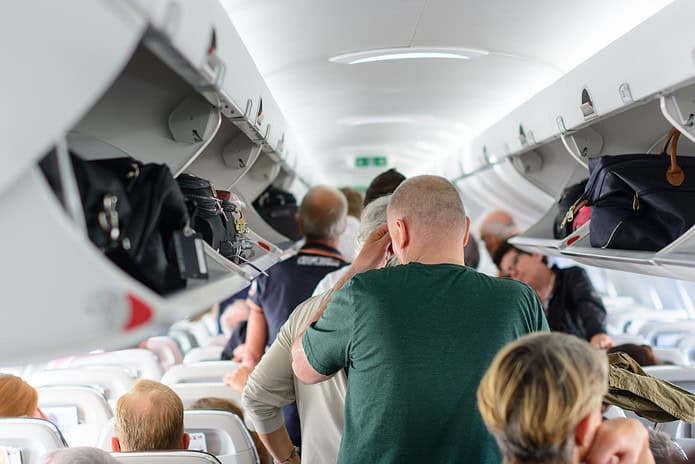 People are standing and sitting in an airplane cabin before unborading