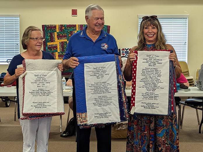 Alice Reid, William Stoehs and Mary Ann Delvalle show the embroidered labels on their quilts listing military accomplishments [Credit: Julie Maglio]