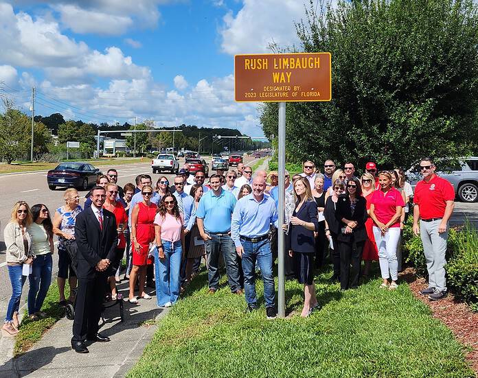 Community members, officials and stakeholders gather around the sign commemorating Rush Limbaugh Way in Brooksville on Thursday. [Credit: Austyn Szempruch]