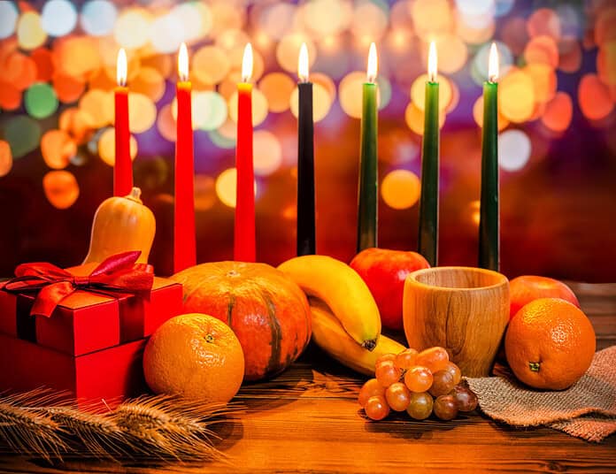 Kwanzaa holiday concept with decorate seven candles red, black and green, gift box, pumpkin, bowl and fruit on light blur bokeh background