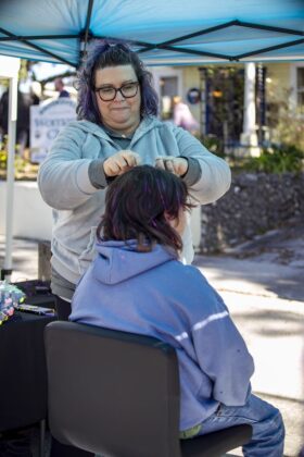 Heather Boodhram weaves hair sparkles into a kid's hair at Booksville Festival in Brooksville, Fla., on Saturday, January 25, 2025. (Photo by Hanna Maglio)