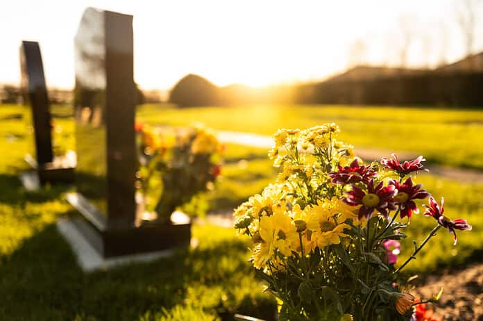 Dusk at a winter's English cemetery seen with in-focus flowers in a burial plot. A number of fresh marble headstones can be seen.