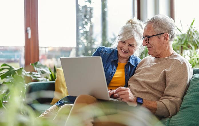 Senior couple using laptop while sitting on sofa in living room at home.